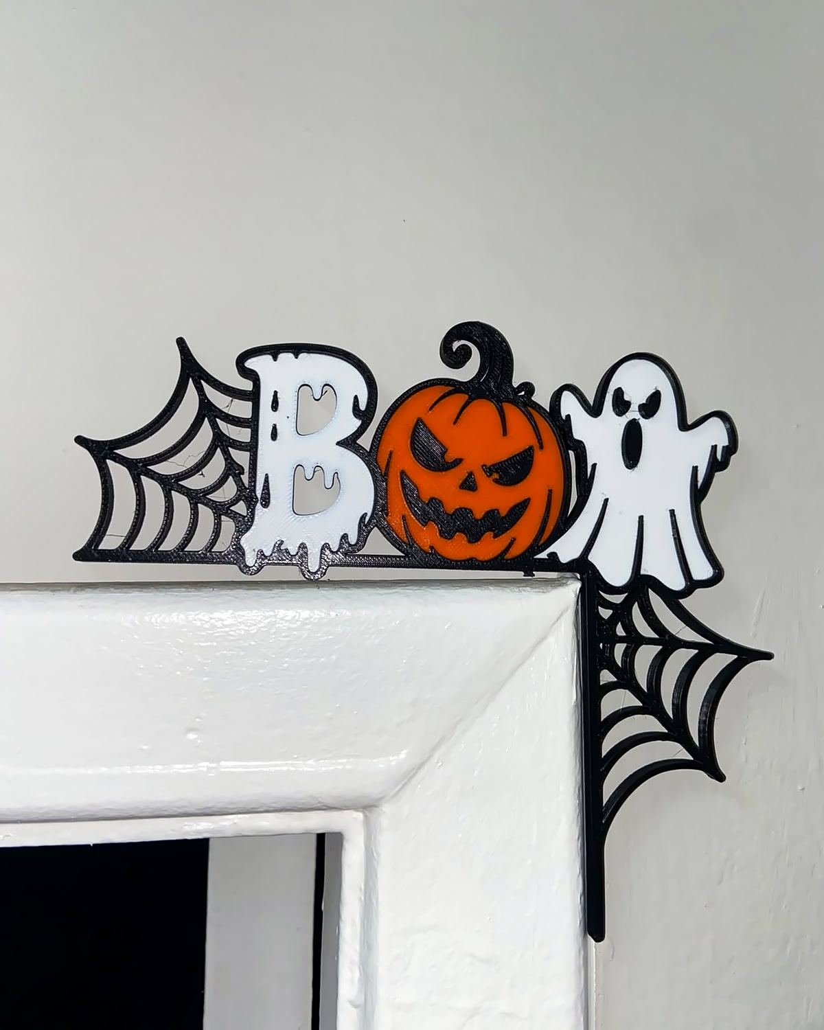 Enfeite de porta de Halloween escrito BOO, com abóbora, fantasma e teias de aranha, encaixado no canto do batente